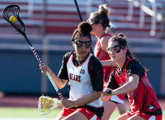 Two lacrosse players in red and white uniforms practice on the field